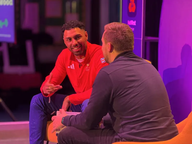 Leon Greenwood seated on stage in a red Team GB jacket, talking with an interviewer