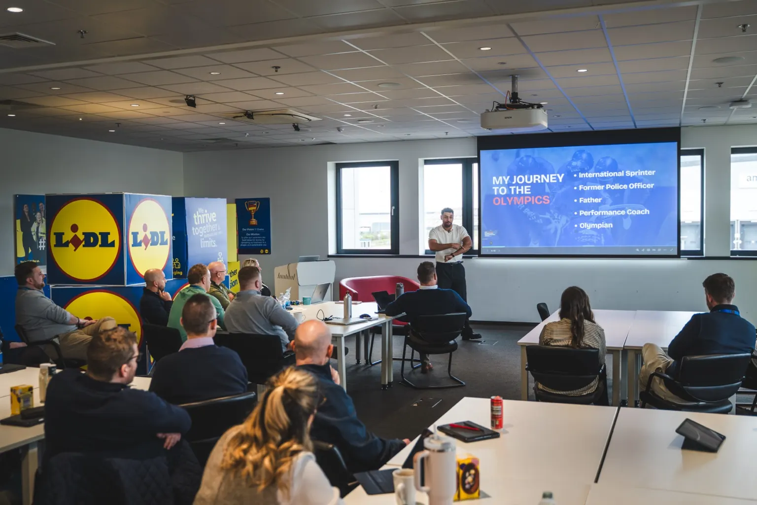 Leon Greenwood presenting to a room of corporate delegates at Lidl, with a slide titled My Journey to the Olympics