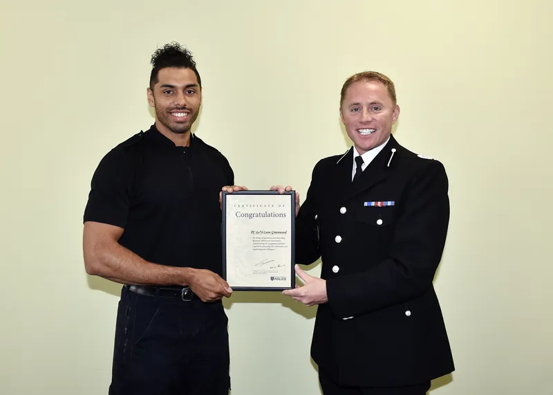Leon Greenwood in Thames Valley Police uniform, holding a framed certificate alongside a senior officer